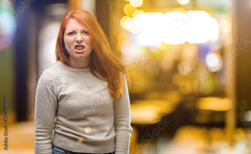 Beautiful young redhead woman angry and stressful frowns face in dissatisfaction, irritated and annoyed, expressing anger at night