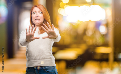 Beautiful young redhead woman disgusted and angry, keeping hands in stop gesture, as a defense, shouting at night