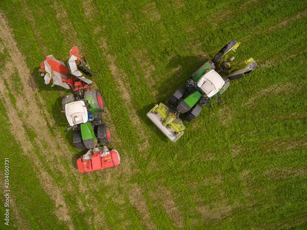 Aerial view of two tractor mowing a green fresh grass field, 
 farmer in a modern tractors mowing a green fresh grass field on a sunny day