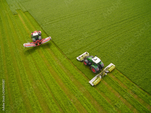 Aerial view of two tractor mowing a green fresh grass field, farmer in a modern tractors mowing a green fresh grass field on a sunny day