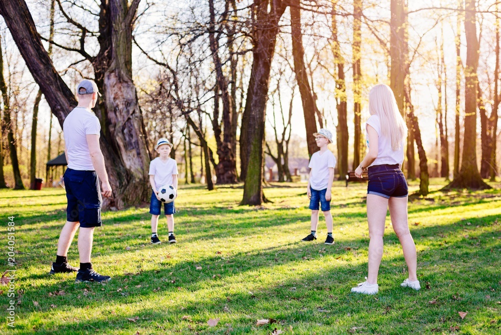 Family throwing ball on green grass in park.