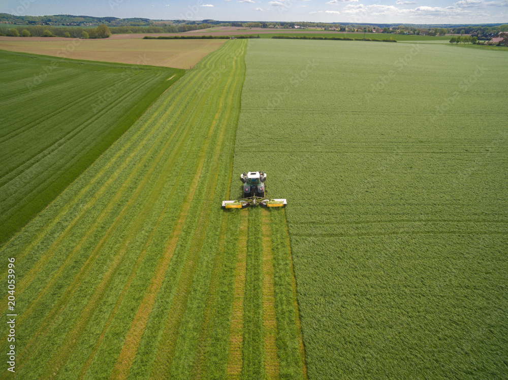 Aerial view of a farmer in a modern tractor mowing a green fresh grass field on a sunny day with blue sky.
Aerial view of a farmer in a modern tractor mowing a green fresh grass field on a sunny day with blue sky.