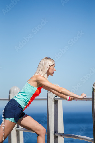 Beautiful blond female fitness athlete stretching before her outdoor run next to the ocean