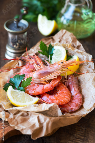 Fresh raw shrimps on parchment paper against rustic wooden background with lemon wedges and parsley
