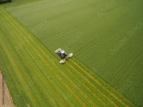 Aerial view of a tractor mowing a green fresh grass field, 
a farmer in a modern tractor mowing a green fresh grass field on a sunny day
