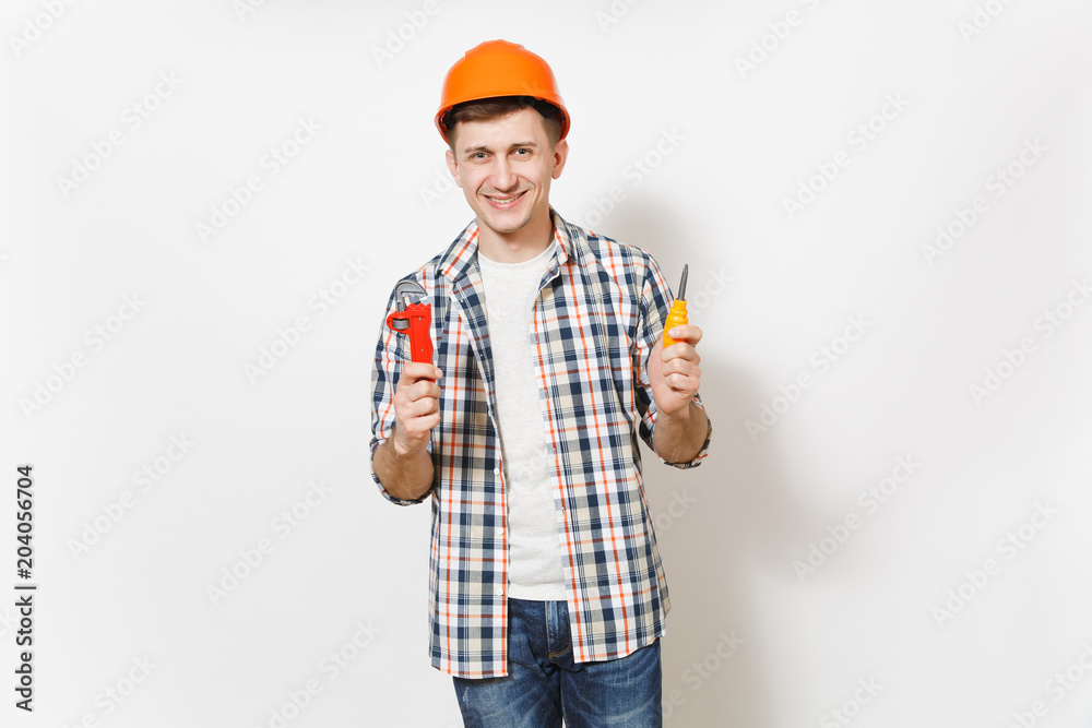 Young smiling handsome man in protective orange hardhat holding toy screwdriver and adjustable wrench isolated on white background. Instruments for renovation apartment room. Repair home concept.