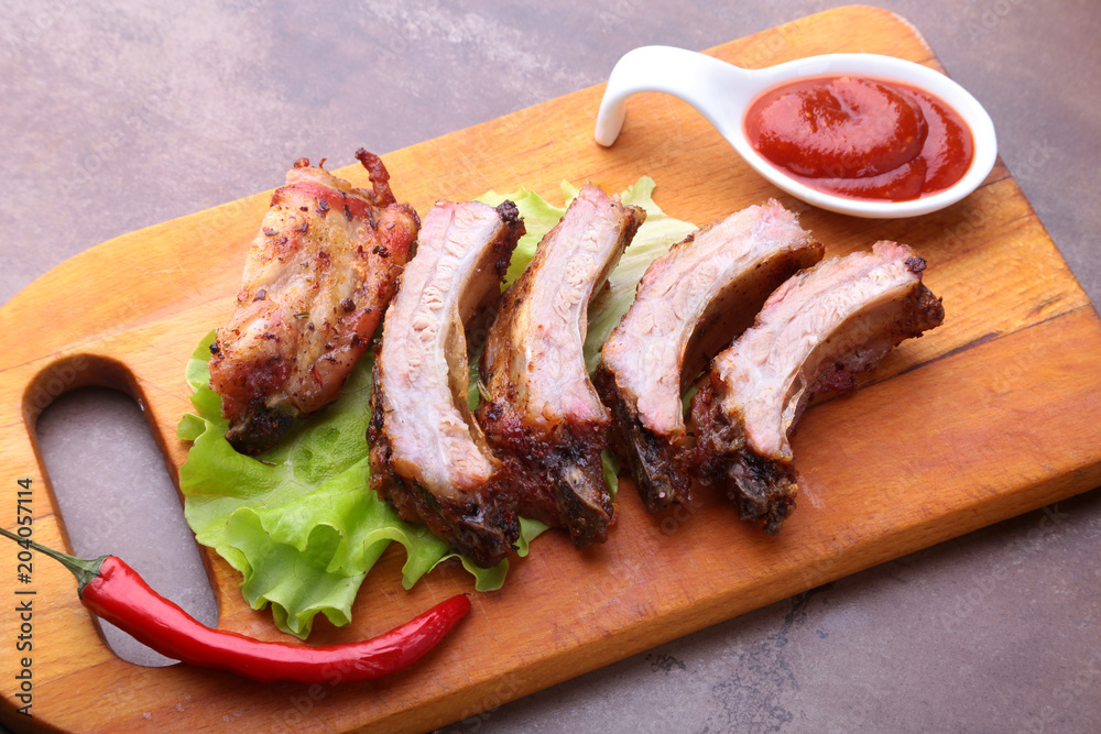 grilled barbecued ribs with lettuce leaves, hot chili pepper and sauce on wooden cutting board. grilled barbecued ribs with lettuce leaves, hot chili pepper and sauce on wooden cutting board.