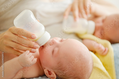 Mother of twin babies feeding them with artificial nutrition. Breast feeding vs bottle feeding concept. Nursing twins.
