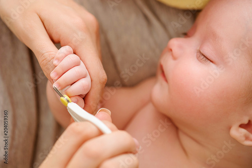 Baby getting fingernails cut while sleeping by his mother with scissors. Nursing a child. How to successfully clip your baby’s nails