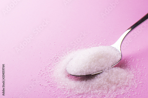spoon with sugar on a pink background, side view