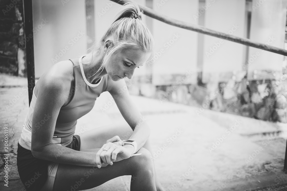 Beautiful blond female fitness model resting on some stairs and checking her heart rate monitor to monitor her exercise