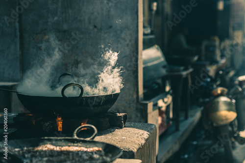 Street food in India cooking in fatiscent big pan or wok in a small street food stall. White smoke coming out from the pan, teal toned image.