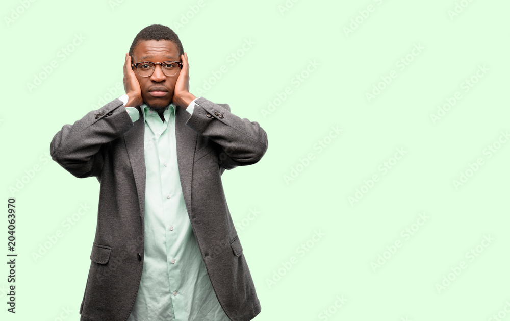 African black man wearing jacket covering ears ignoring annoying loud noise, plugs ears to avoid hearing sound. Noisy music is a problem. African black man wearing jacket covering ears ignoring annoying loud noise, plugs ears to avoid hearing sound. Noisy music is a problem.