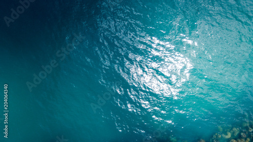 Aerial: overhead view of transparent blue sea surface against the coral line and bottom