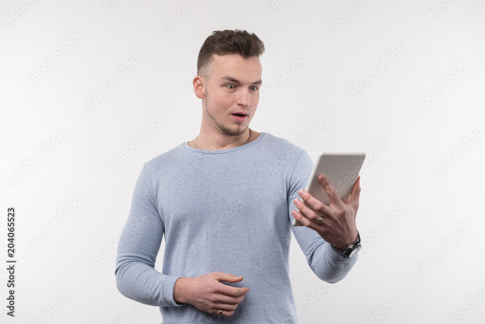 What is this. Pleasant young man expressing his surprise while looking at the tablet screen What is this. Pleasant young man expressing his surprise while looking at the tablet screen