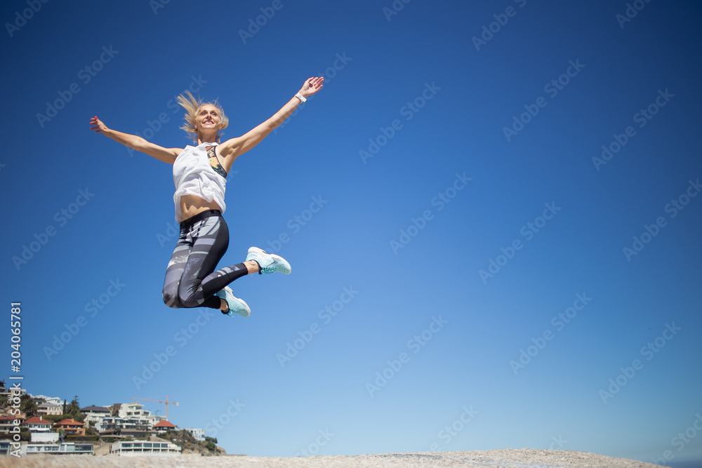 Beautiful blond female fitness model jumping for joy against a bright blue sky Beautiful blond female fitness model jumping for joy against a bright blue sky