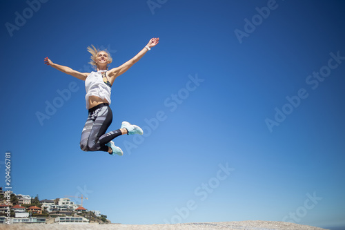 Beautiful blond female fitness model jumping for joy against a bright blue sky