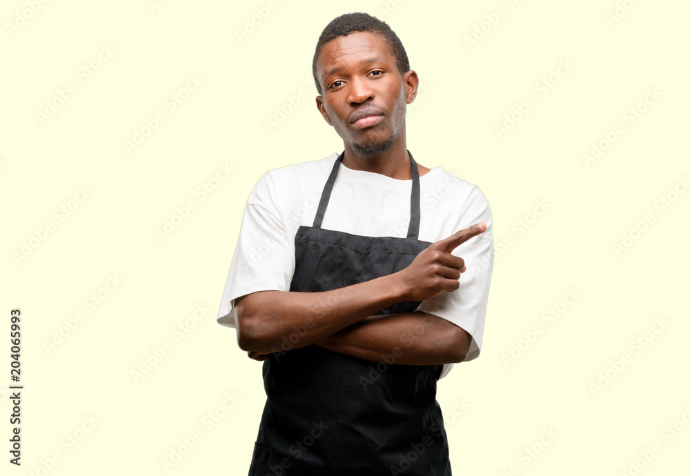 African man shop owner wearing apron pointing away side with finger African man shop owner wearing apron pointing away side with finger