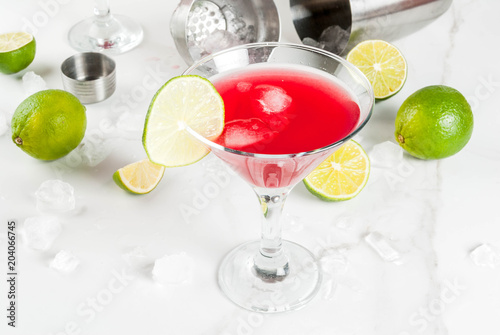 Red cosmopolitan cocktail with lime in martini glass, on white marble background copy space photo