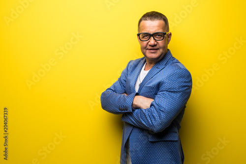 Portrait of happy fun middle age man in suit and eyesglasses isolated on yellow background
