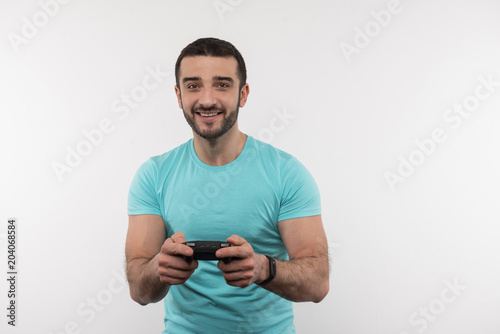 Interesting entertainment. Joyful bearded man holding a video game console while having fun at home © zinkevych