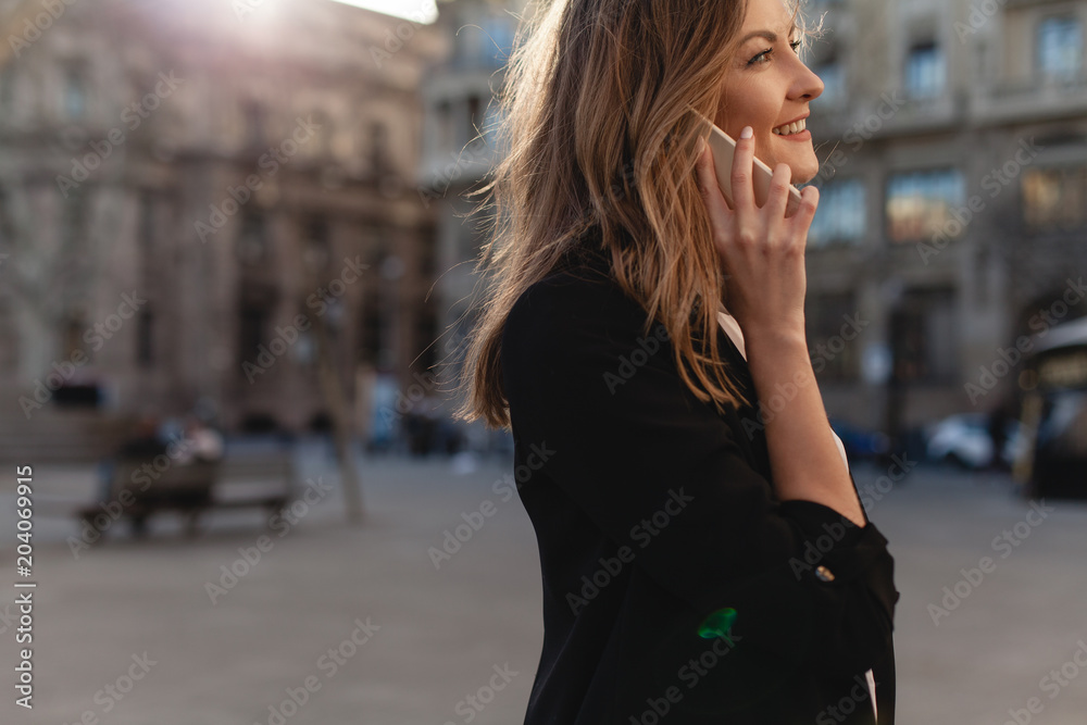 Fototapeta premium Happy successful businesswoman calling with cell telephone outside, smiling female entrepreneur managing business talking via mobile phone and walking on the city street, making phone call after job