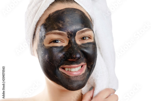  close-up portrait beautiful woman with facial black mask on white background, girl with a white towel on her head, satisfied and happy smile