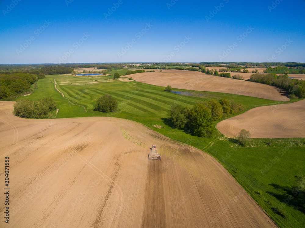 Obraz premium aerial view - a modern tractor working on the agricultural field - tractor plowing and sowing in the agricultural field - high top view