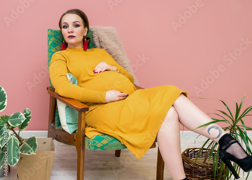 Beautiful fashionable pregnant woman sitting in a chair