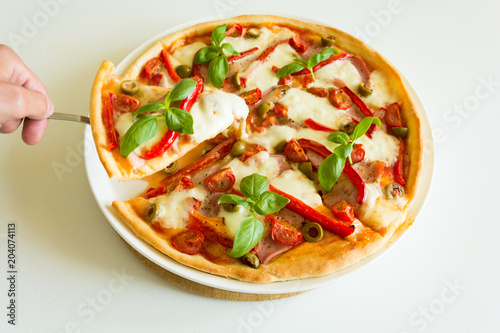 Fresh pizza with tomatoes, cheese mozzarella, red pepper and olives decorated basil leaves on white wooden table. Close up 