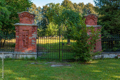 stara brama do parku przy cerkwi prawosławnej w Białowiezy. w oddali widać pasiekę z kilku kolorowych drewnianych uli