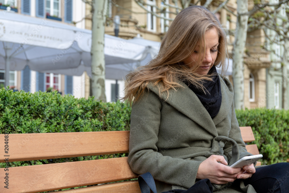 Young woman sitting on park bench with smartphone
