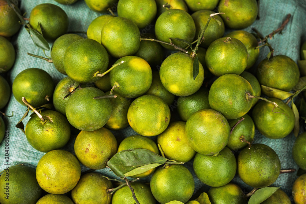 Pile of green unripe oranges background. Many tropical citrus fruit for sale at a food market
