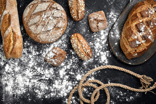 Homemade rye bread sprinkled with flour and various grains and seeds on a black background with spikelets of wheat or rye and oats.
