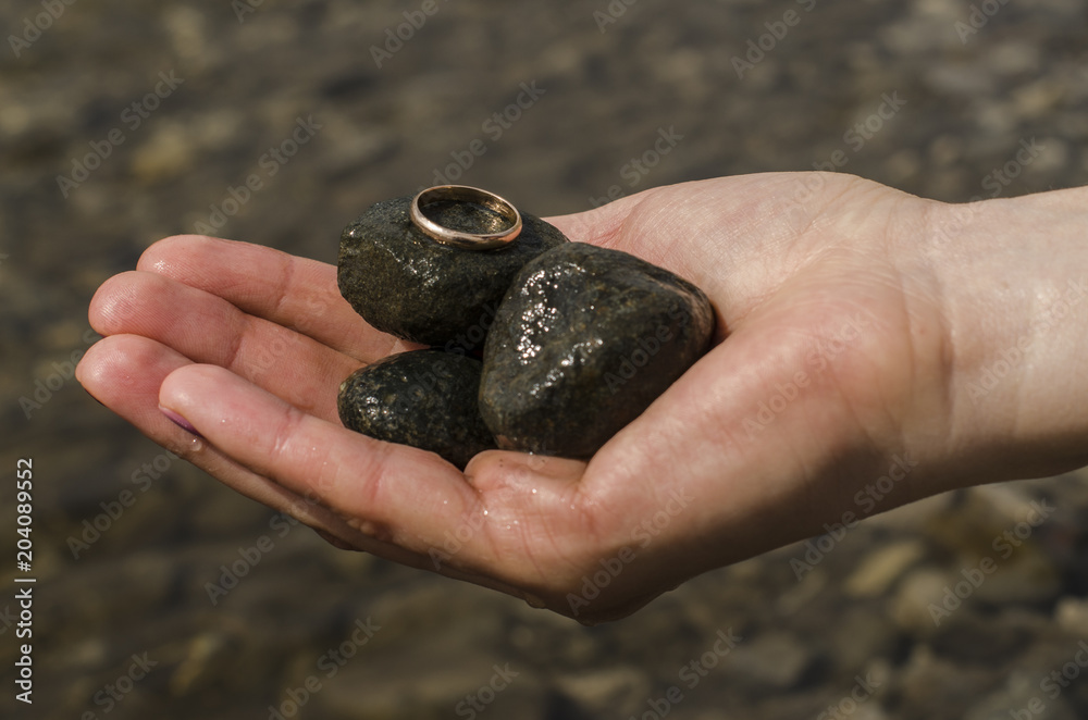 A female hand holds river stones and a gold wedding ring A female hand holds river stones and a gold wedding ring