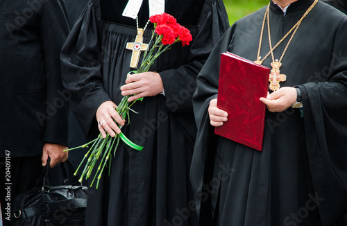 Two priests standing next to each other on the ceremony. One of them is holding flowers and another one a folder