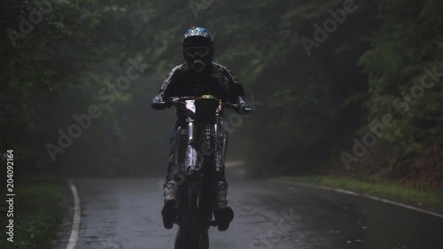 Shot of the Professional Motocross Driver Riding on His FMX Motorcycle on the rear wheel in the rain 4k