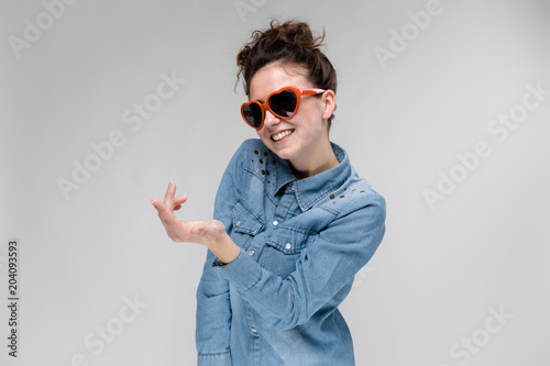 Young brunette girl with glasses in the form of a heart. The hairs are gathered in a bun. The girl holds out her hand. photo