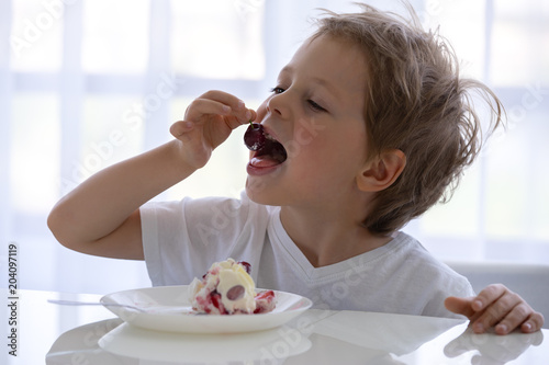 child in the kitchen eating a cake with cream and berries is very appetizing