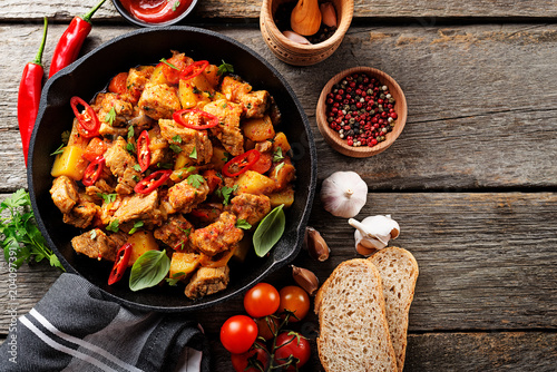 Traditional goulash stewed meat with potatoes, carrots and vegetables in a cast-iron frying pan on a dark wooden background. top view. photo