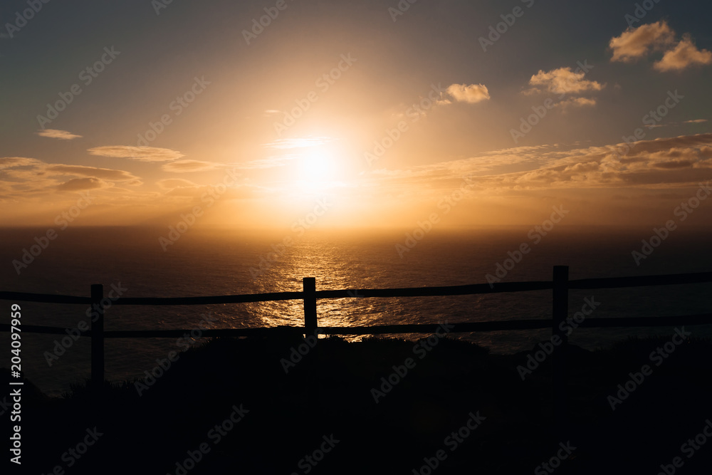 the glare of the sun on the water. high coast with a wooden fence overlooking the evening sea. beautiful sunset
