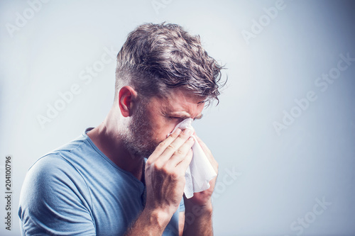 Man sneezing in a tissue outdoors. Pollen allergy, Springtime. photo