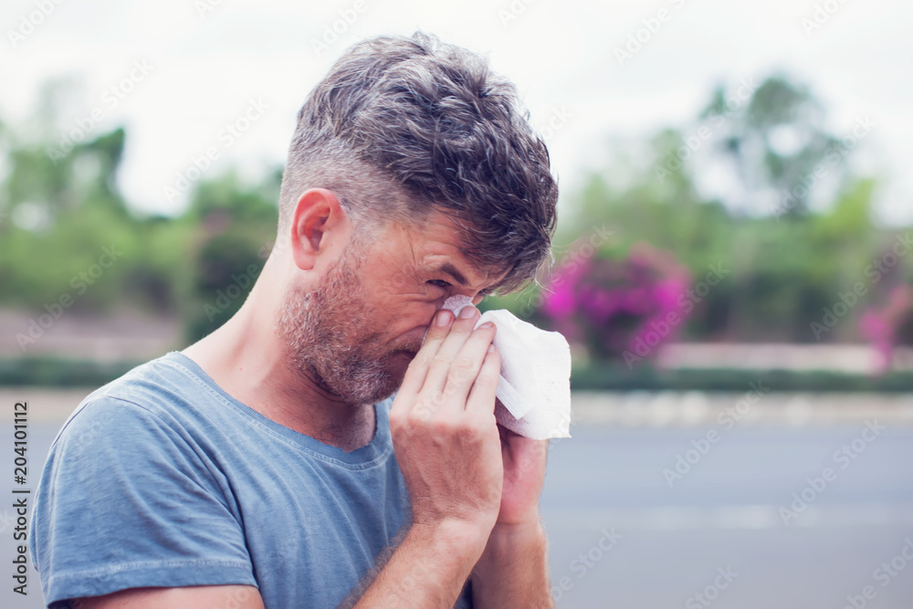 Man sneezing in a tissue outdoors. Pollen allergy, Springtime. Man sneezing in a tissue outdoors. Pollen allergy, Springtime.