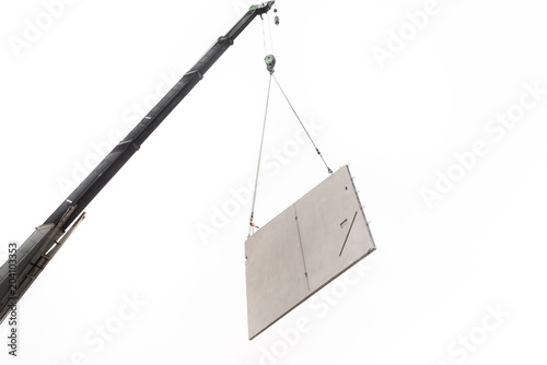 Construction site crane is lifting a precast concrete wall panel.