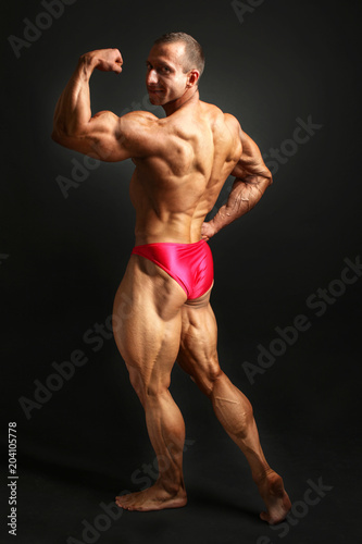 Studio shot of young male bodybuilder posing, looking back over his shoulder showing back, biceps and legs muscles.