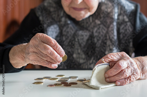 Elderly 95 years old woman sitting miserably at the table at home and counting remaining coins from the pension in her wallet after paying the bills.