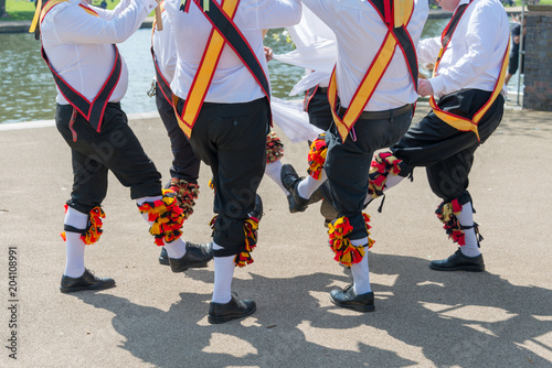 group of morris dancers wearing sashes and bells dance in a circle