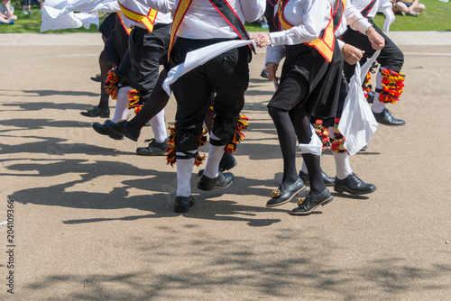 Morris dancers wearing bells and white shirts and stockings dance on May Day Bank Holiday with sticks and handkerchiefs