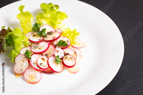 Healthy food organic slices radish salad in white plate on black slate board