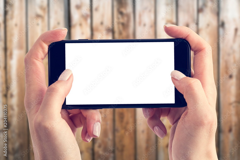 Close up of hands are holding a smartphone with a blank screen and a copy space. Blurred wooden background. Close up of hands are holding a smartphone with a blank screen and a copy space. Blurred wooden background.